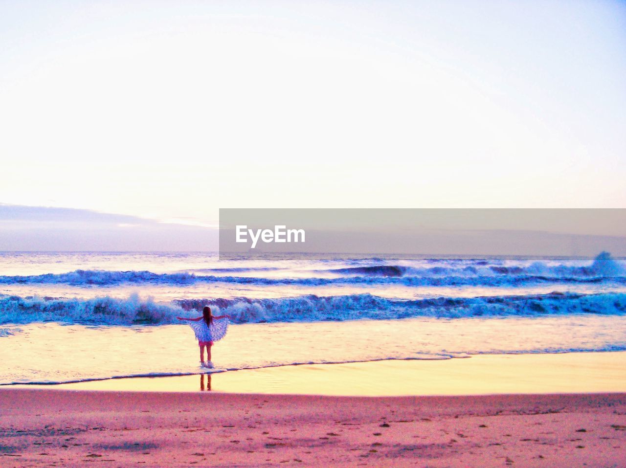 REAR VIEW OF WOMAN STANDING ON BEACH AGAINST SKY