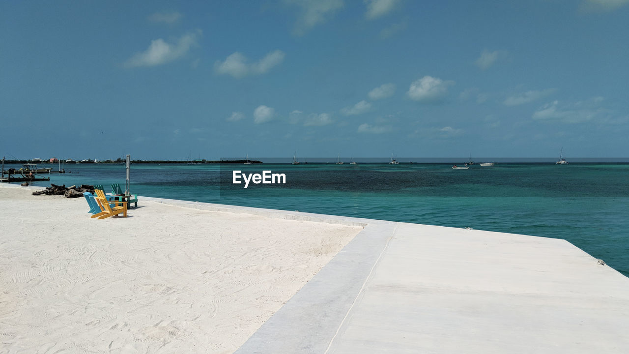 water, sea, sky, land, beach, shore, vacation, ocean, nature, sand, body of water, scenics - nature, beauty in nature, coast, holiday, travel, horizon over water, horizon, trip, travel destinations, cloud, tranquility, day, blue, tranquil scene, tourism, outdoors, bay, sunlight, transportation, summer, idyllic, relaxation, nautical vessel, tropical climate, sunny, wave, chair, architecture, copy space, environment, seascape