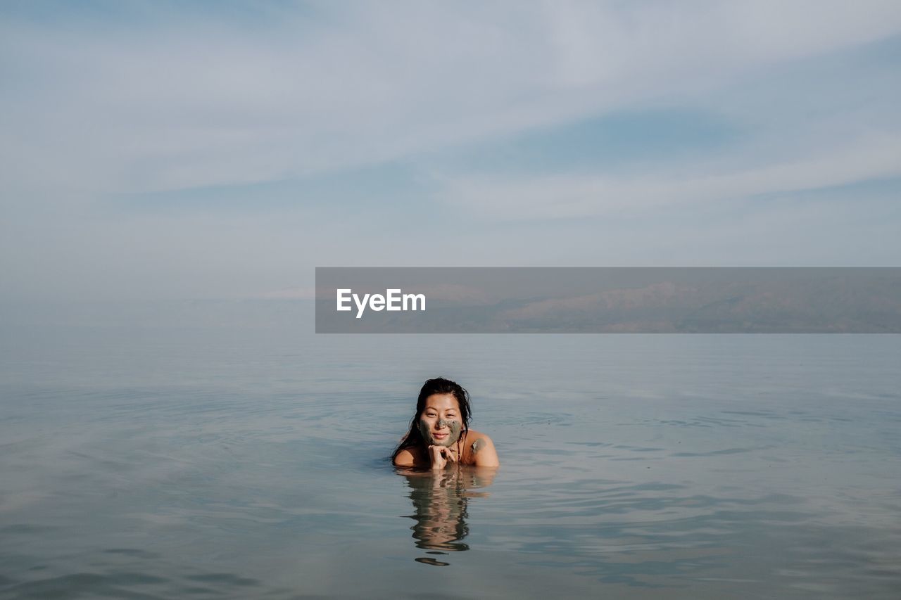 Portrait of young woman swimming in sea against cloudy sky