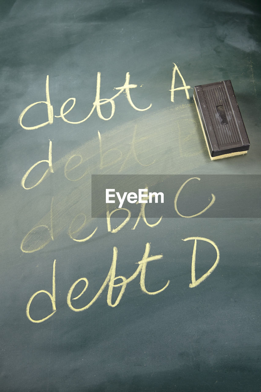 High angle view of debt written by duster on blackboard