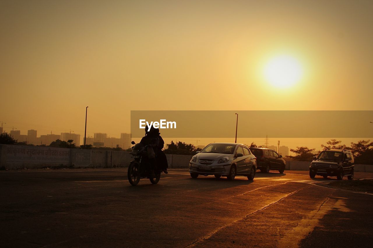 Vehicles on road against sky during sunset