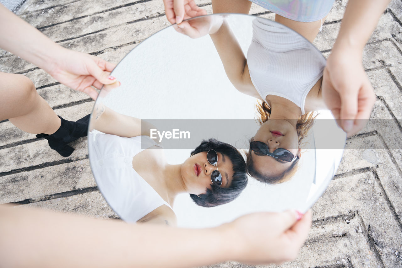 Reflection of lesbian sisters holding mirror outdoors