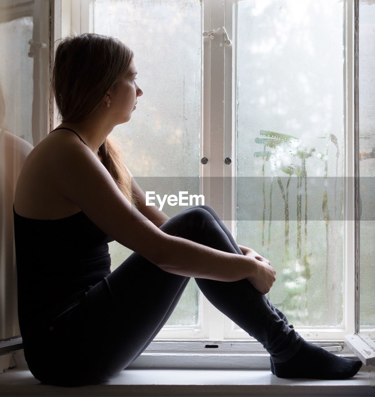 Woman looking through window during monsoon