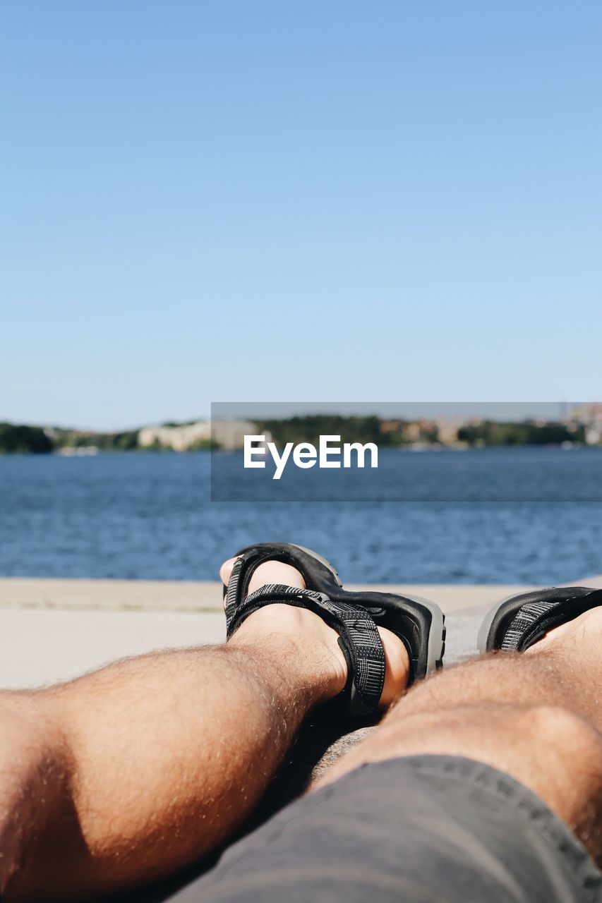 Low section of man relaxing at beach against sky