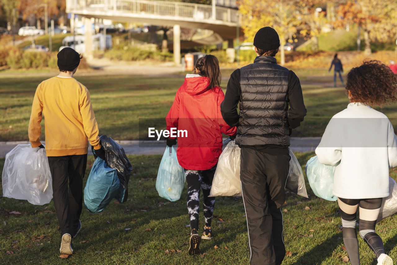 Rear view of young environmentalists walking with plastic waste in park