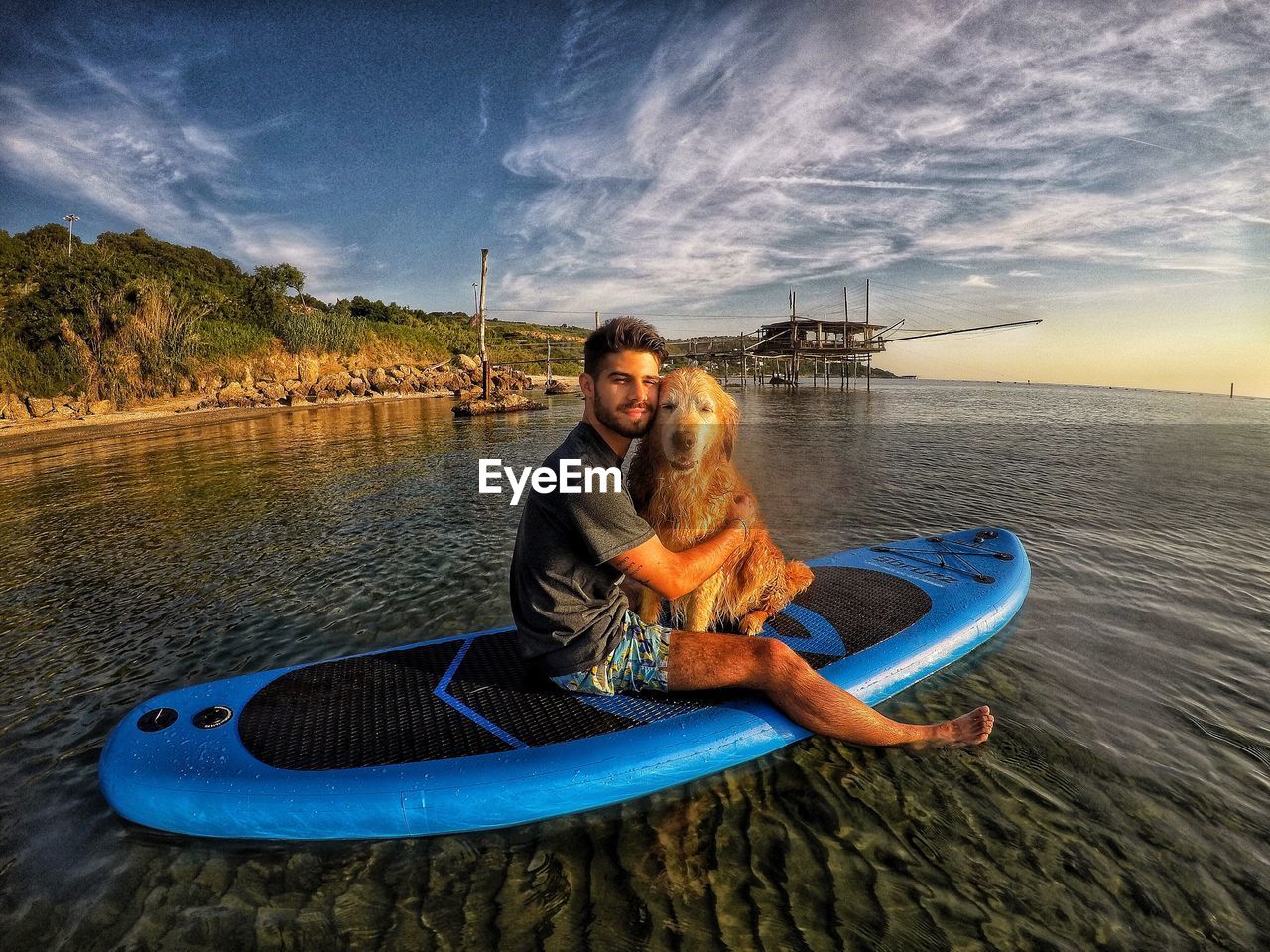 Portrait of man embracing dog on surfboard in sea