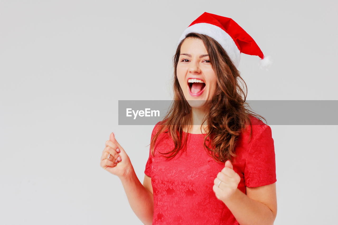 Portrait of young woman wearing santa hat while screaming against gray background