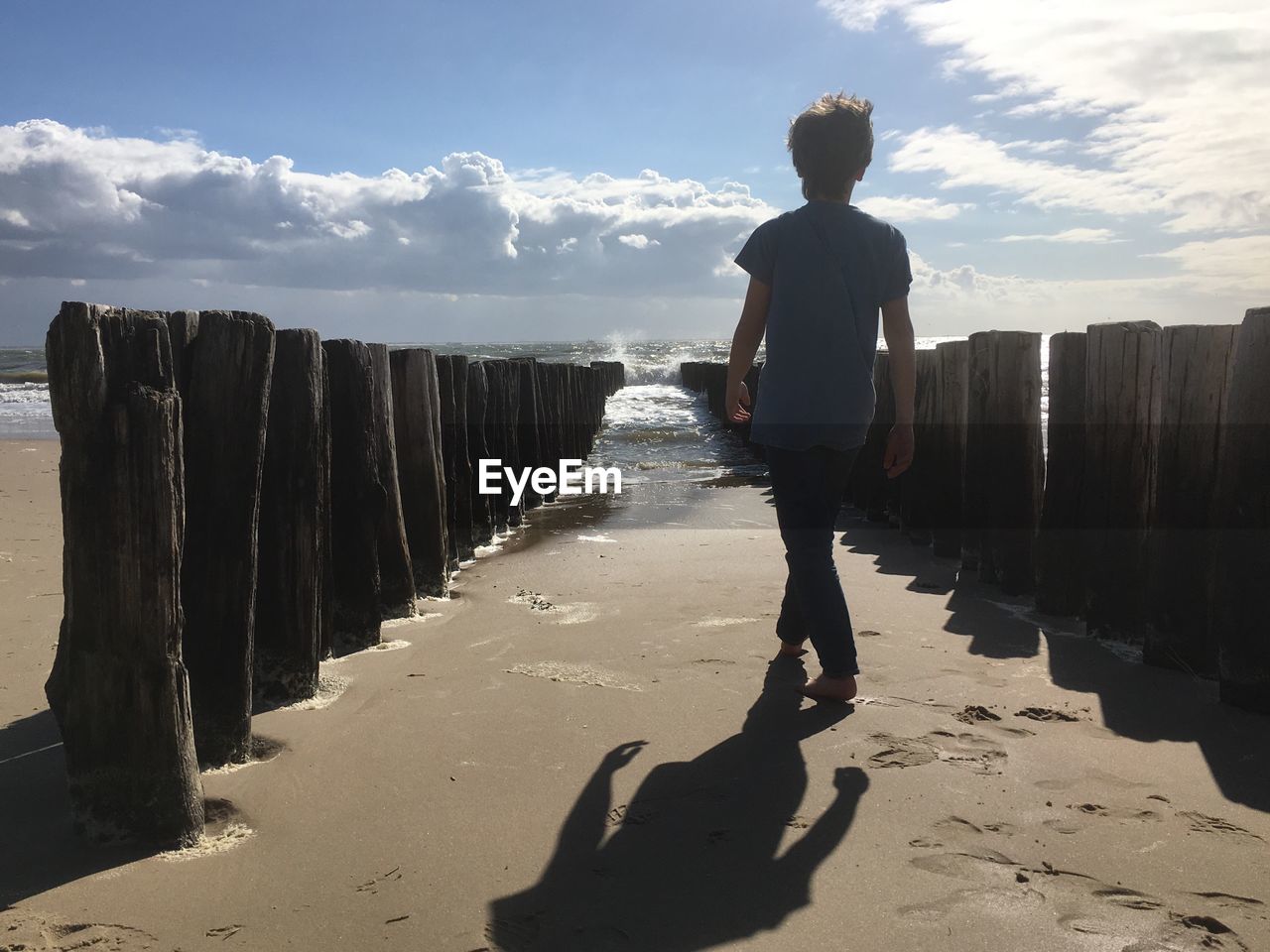 Rear view of man standing on beach against sky