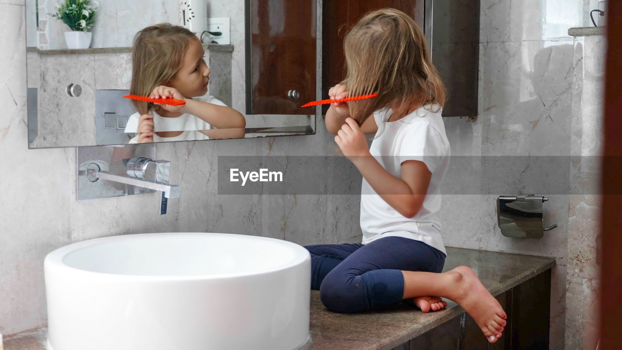 Girl combing hair while looking in mirror