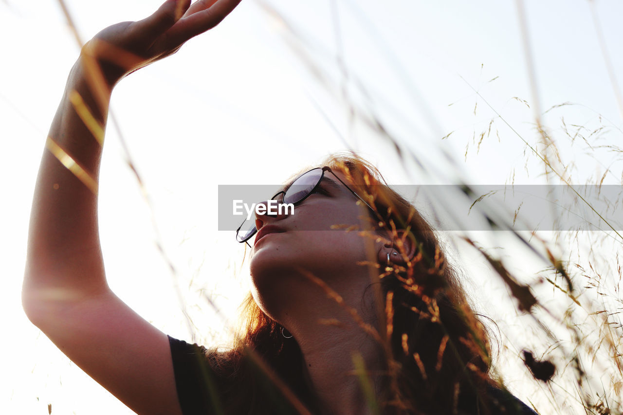 Low angle view of woman shielding eyes against sky