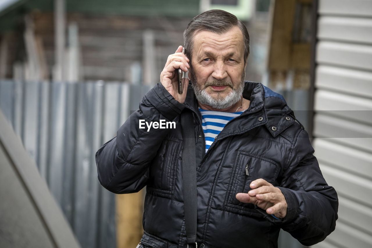 Elderly lonely adult man talking on smartphone outdoors on the street