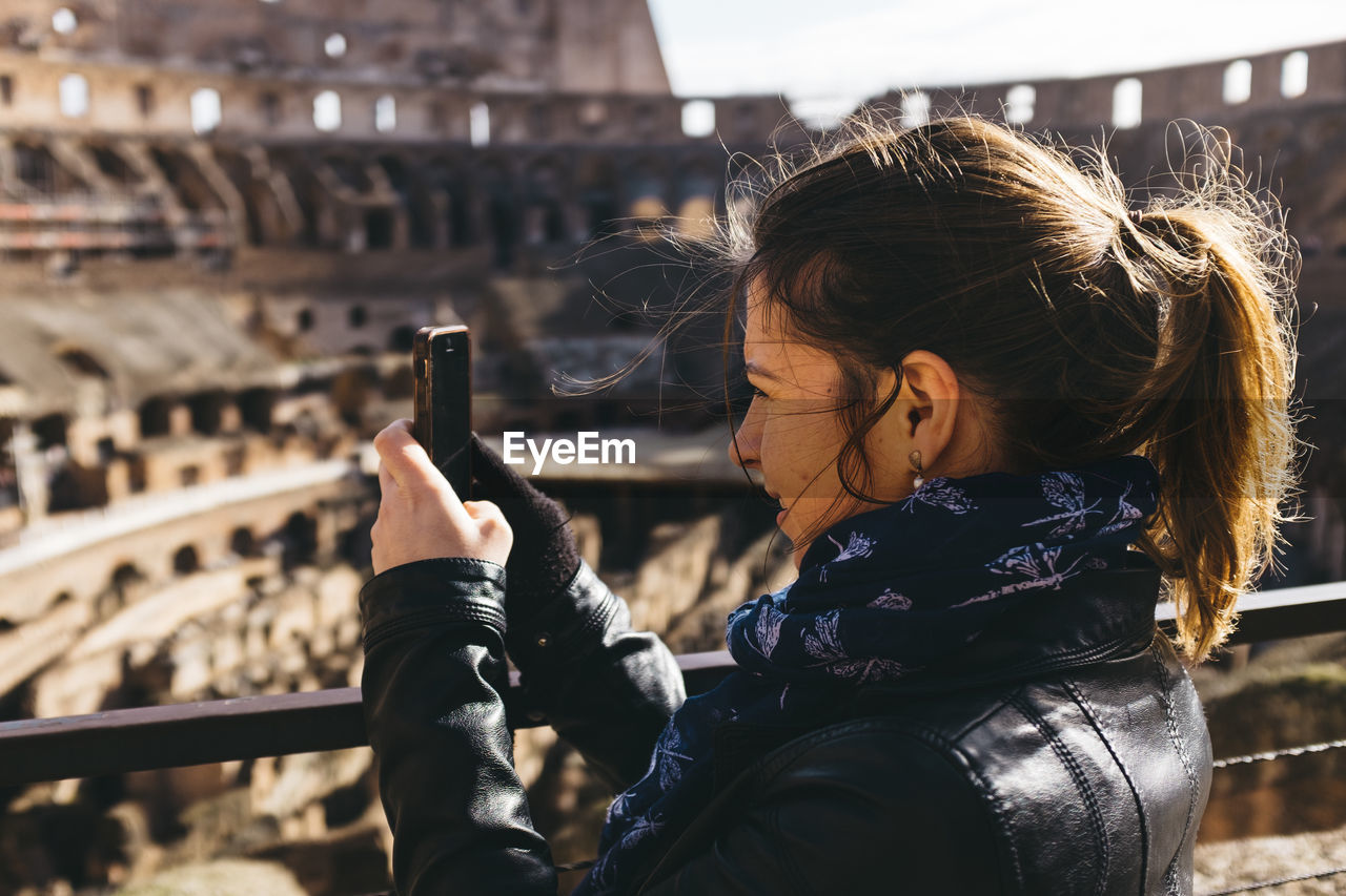 Woman photographing coliseum through smart phone