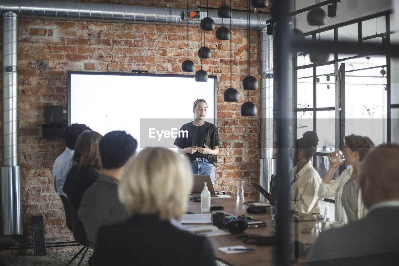 Young businesswoman giving presentation to colleagues during meeting at office