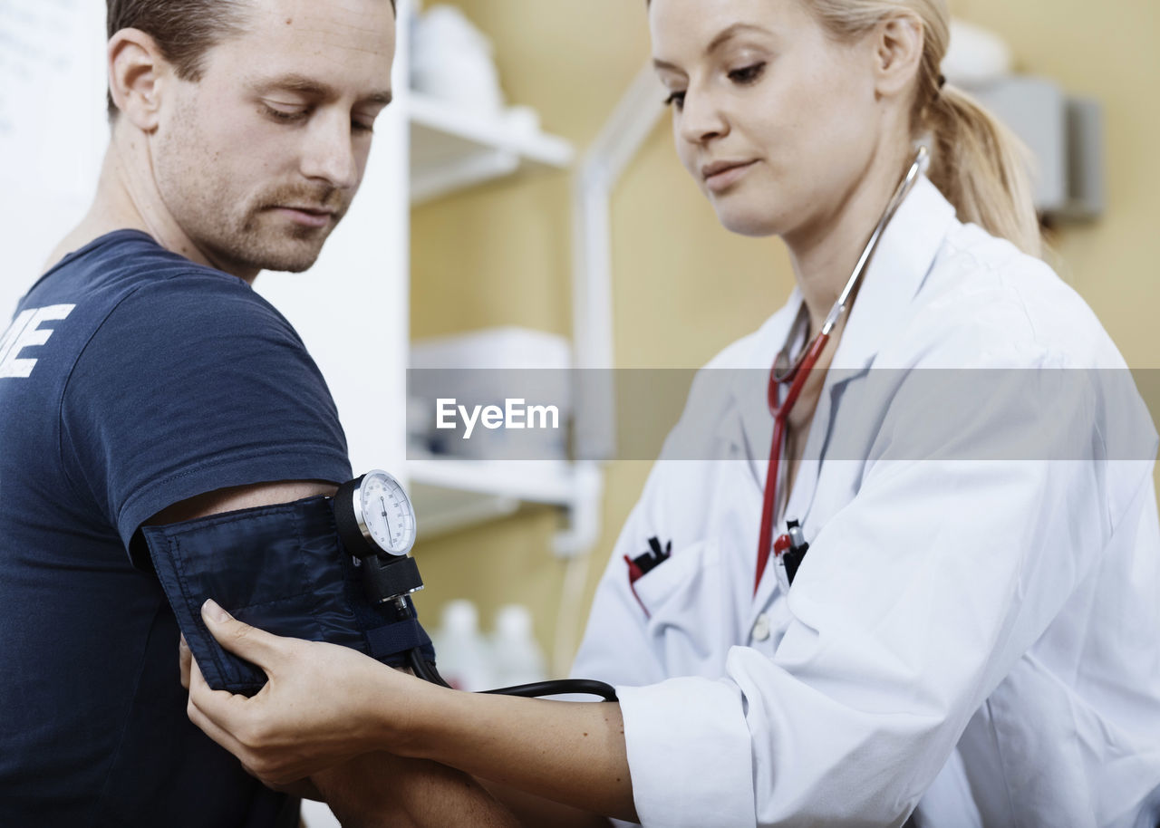 Female doctor wrapping cuff to patient's arm before taking blood pressure in clinic