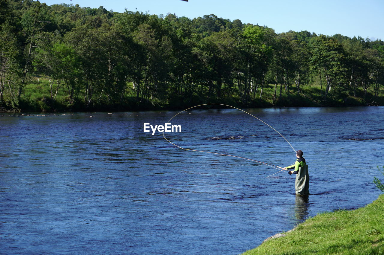 Man fishing in a river against trees