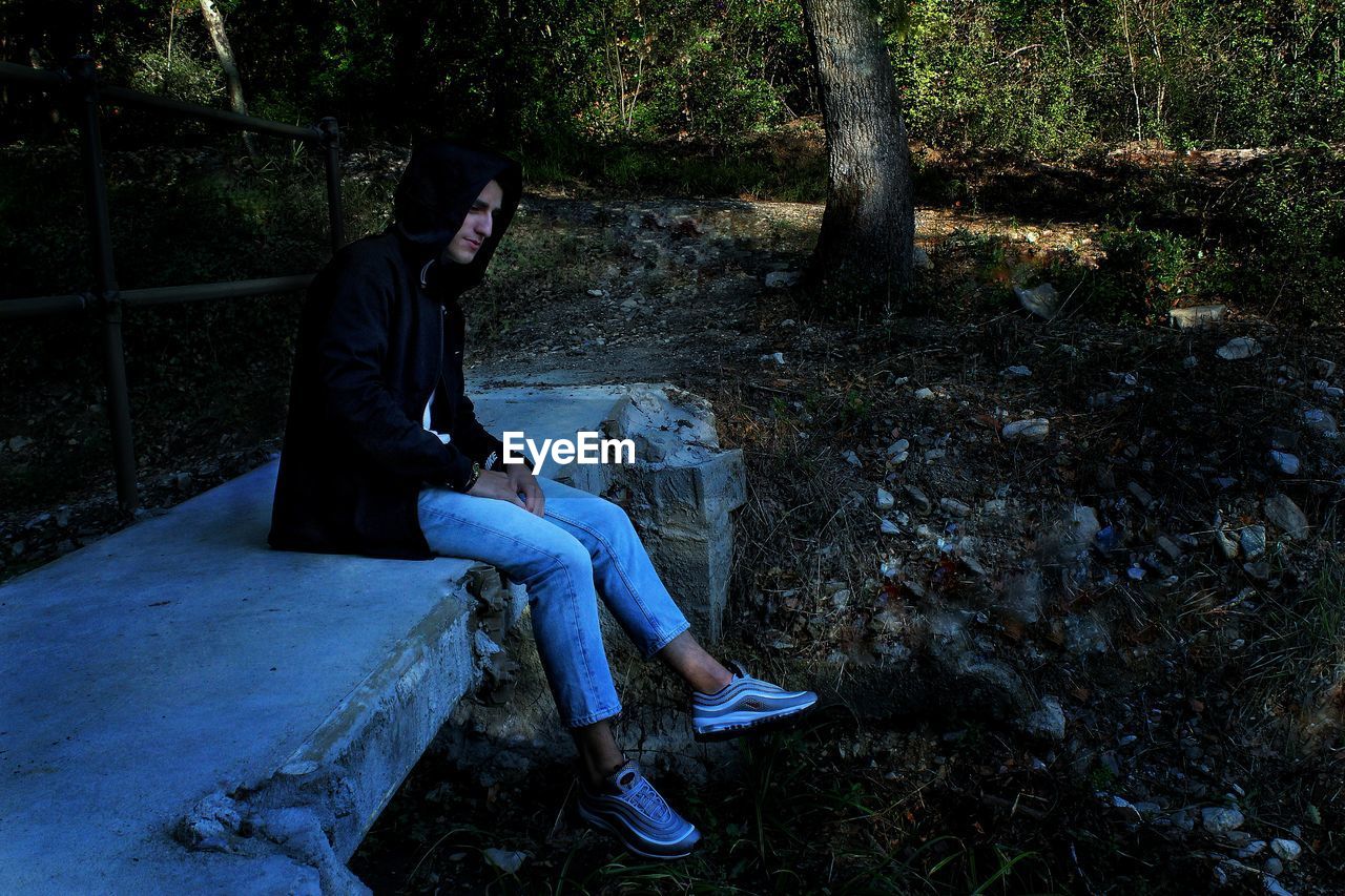 Side view of young man sitting on bridge in forest