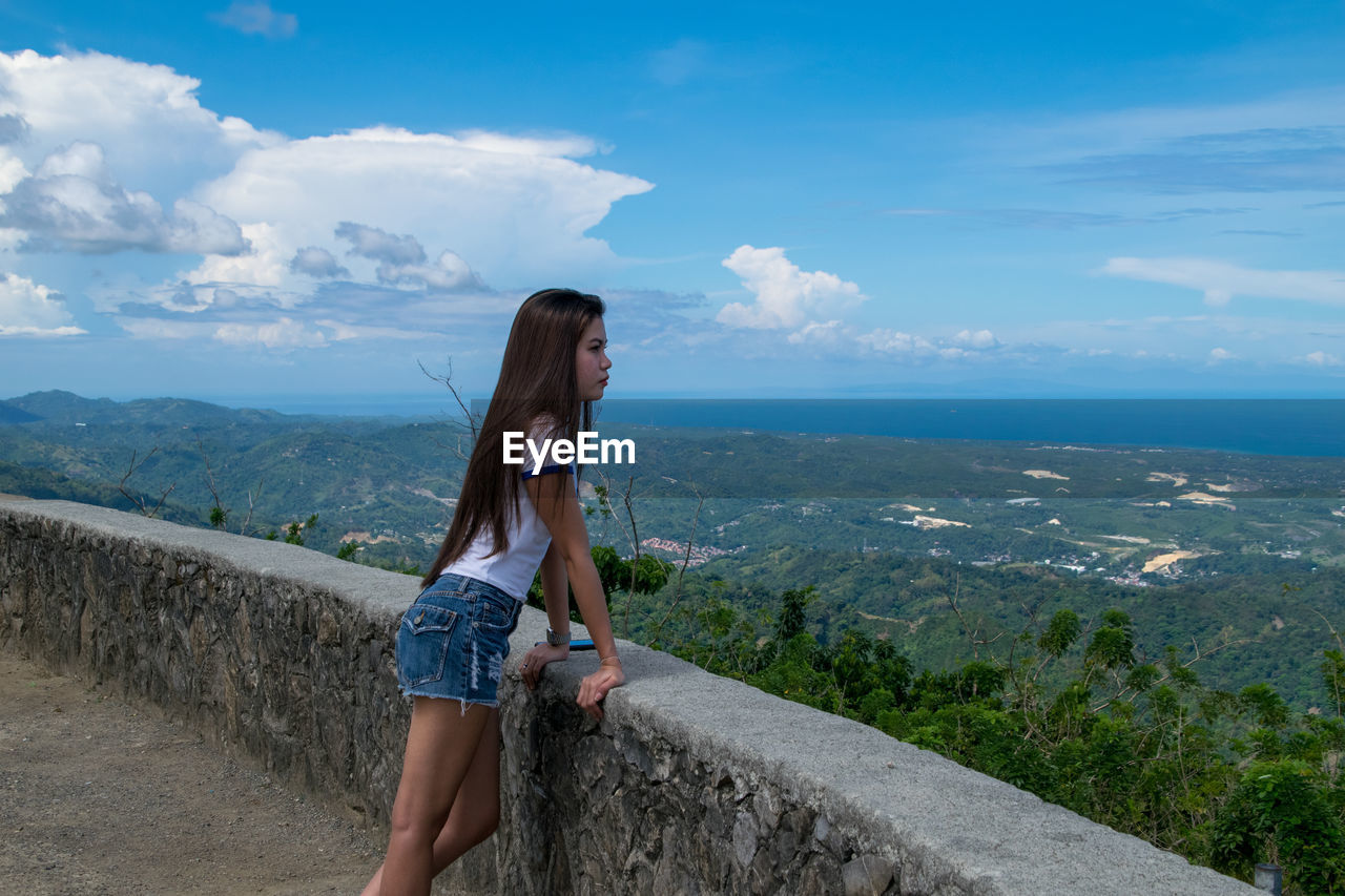 Side view of young woman standing on mountain against sky