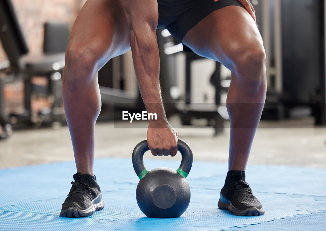 low section of man lifting dumbbell in gym