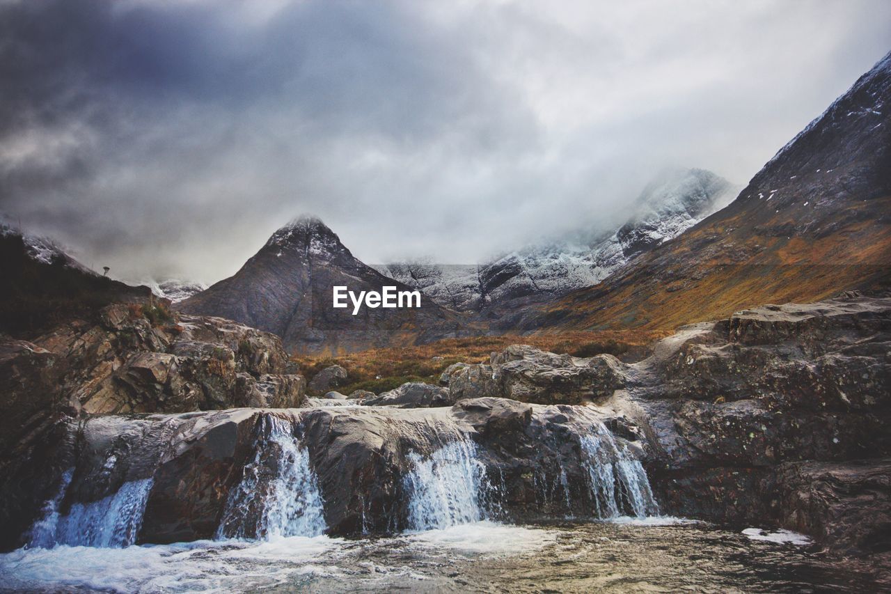 Scenic view of waterfall against cloudy sky