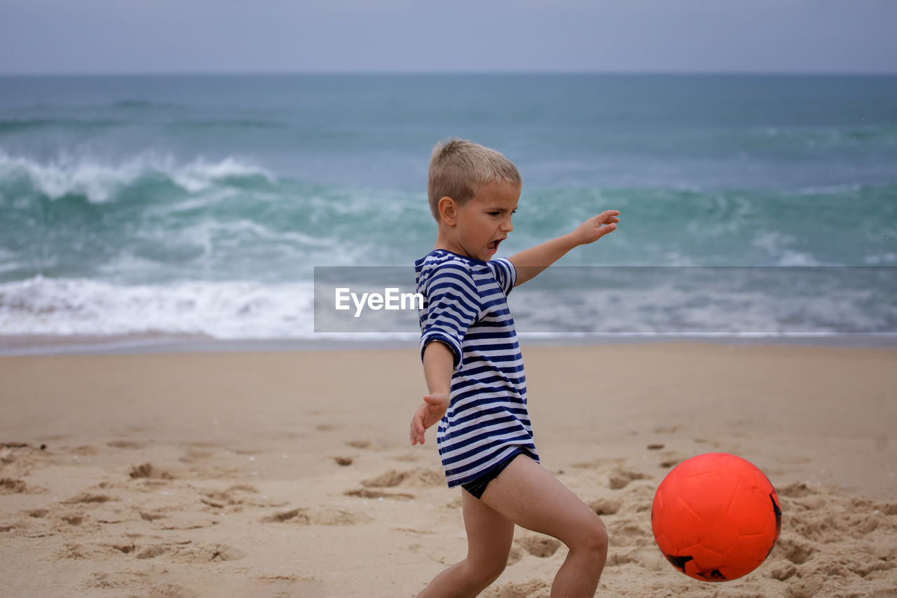 Young soccer player plays barefoot on the ocean shore. football, sport, passion. active lifestyle