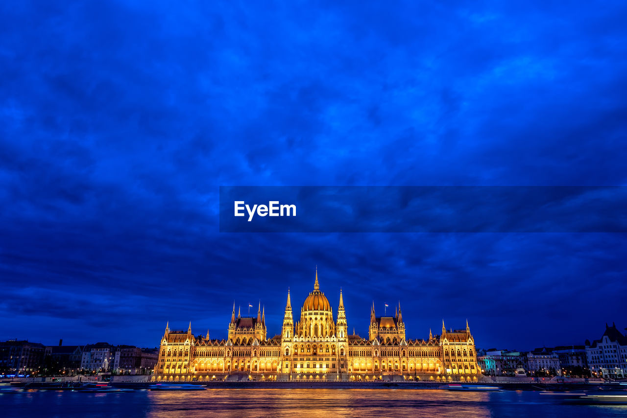 Illuminated hungarian parliament building and danube river in city at dusk