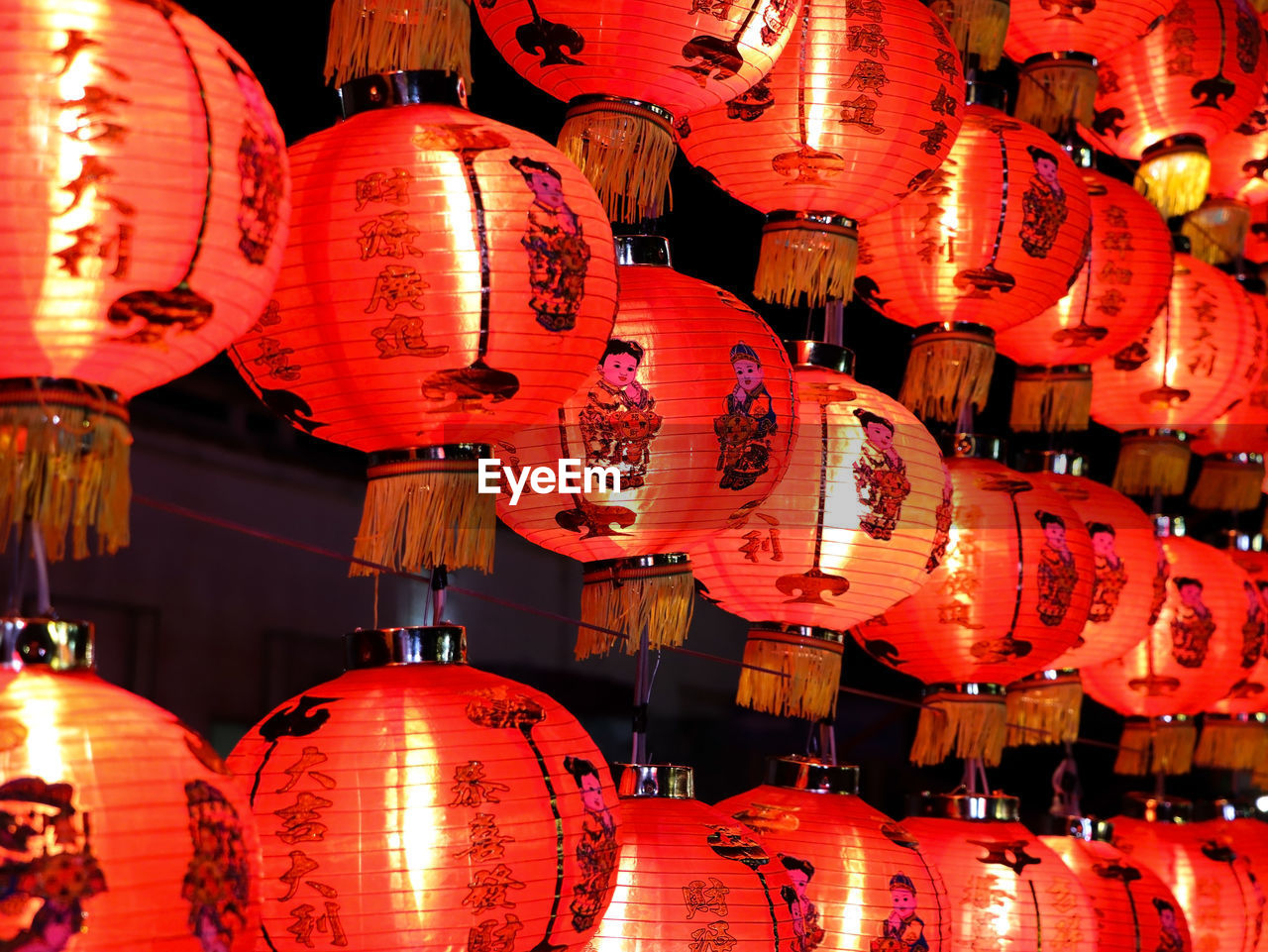 LOW ANGLE VIEW OF ILLUMINATED LANTERNS HANGING IN ROW AT NIGHT