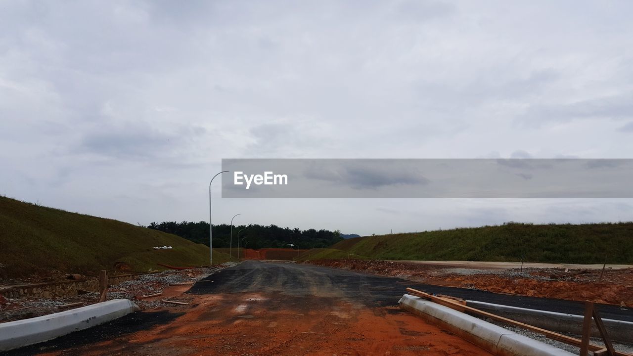 ROAD BY STORM CLOUDS OVER GREEN LANDSCAPE