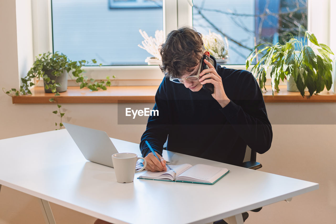 Purposeful  businessman is on the phone with an exiting client, jotting notes in his diary