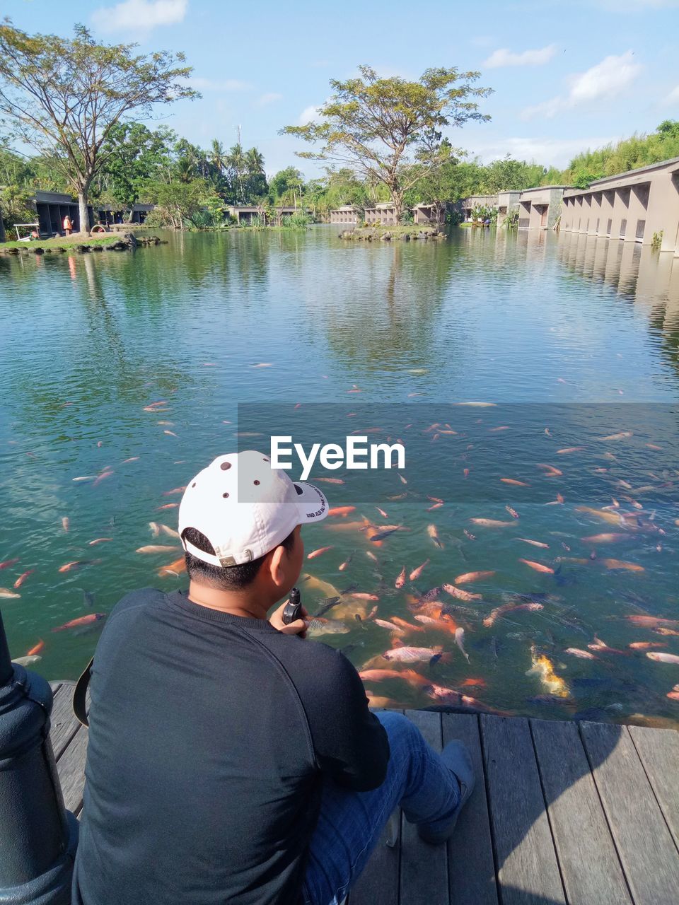 REAR VIEW OF MAN SITTING AT FISH IN LAKE