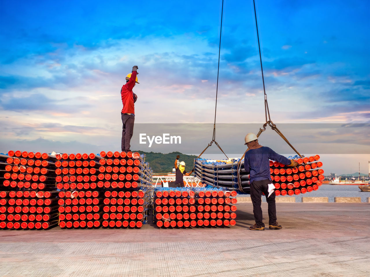 Male workers working with pipes at harbor against blue sky