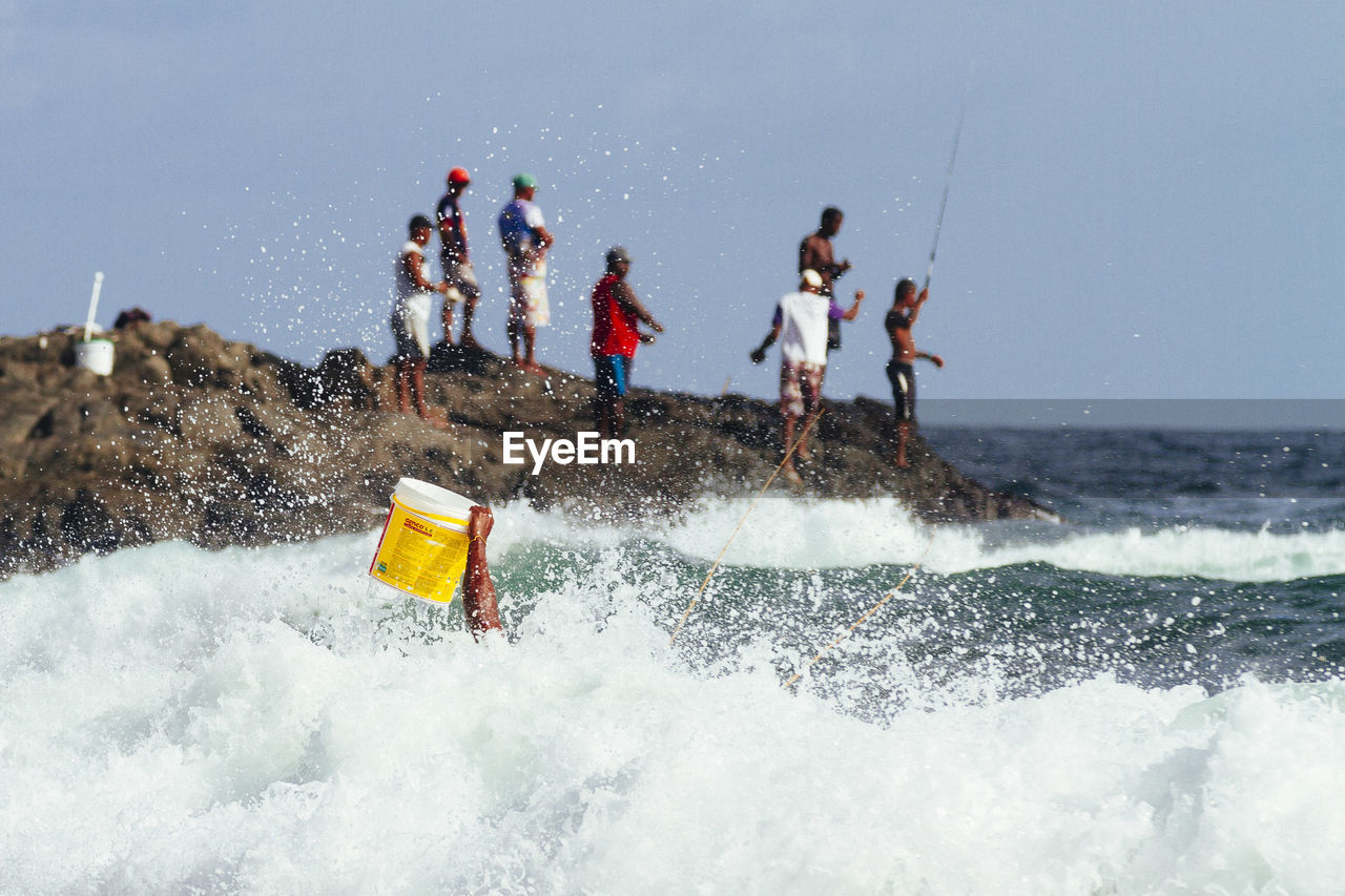 Cropped hand holding bucket in surf with men fishing in background