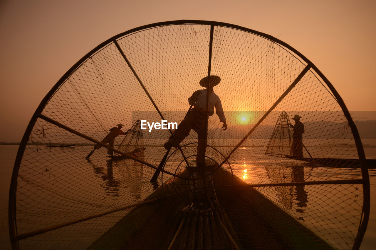 Silhouette men fishing in lake during sunset