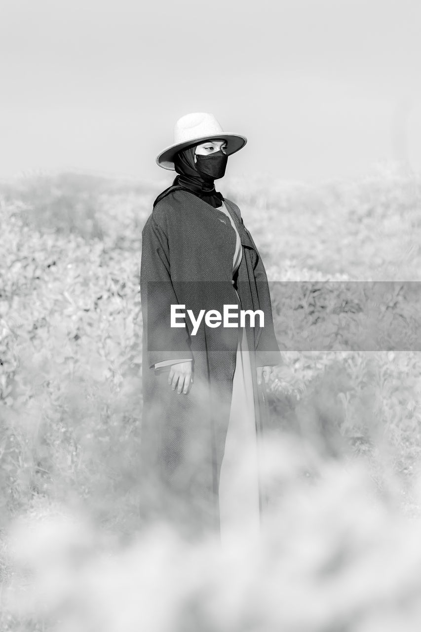 Side view of female  wearing face mask and cowboy hat in the middle of the field