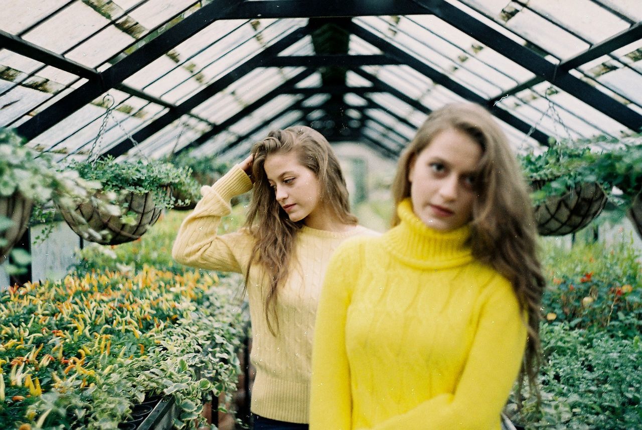 Sisters standing amidst plants in greenhouse