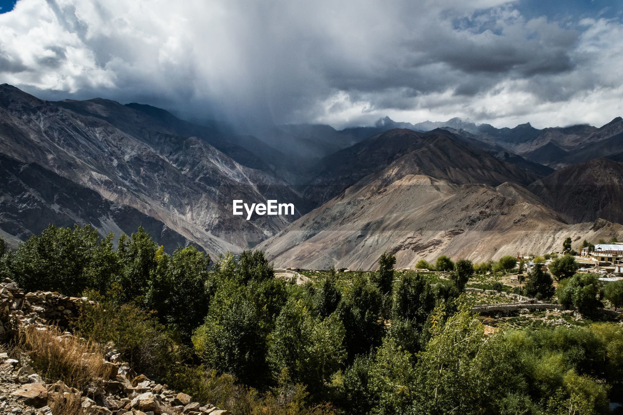 Scenic view of trees by mountain against cloudy sky