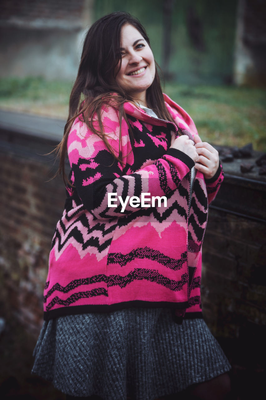 PORTRAIT OF SMILING WOMAN STANDING AGAINST PINK OUTDOORS