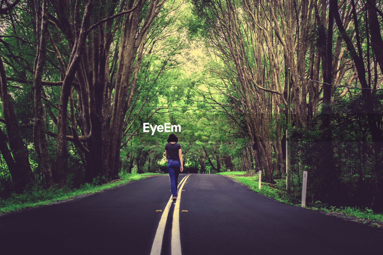 Rear view of woman walking on road in forest