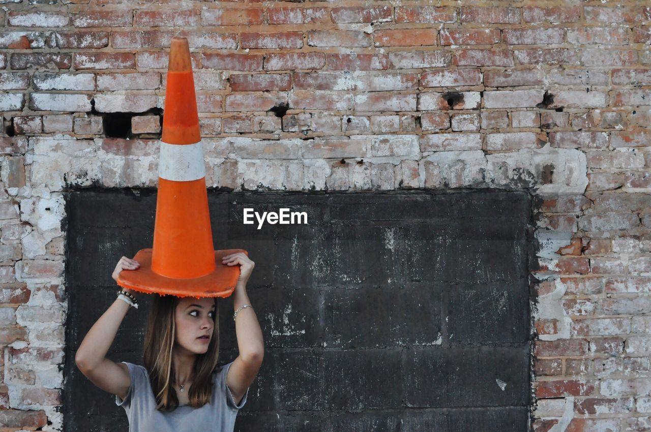 Woman holding traffic cone on head while standing against wall