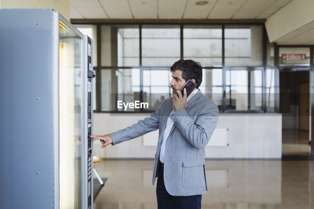 Professor talking on mobile phone while using vending machine in cafeteria at university