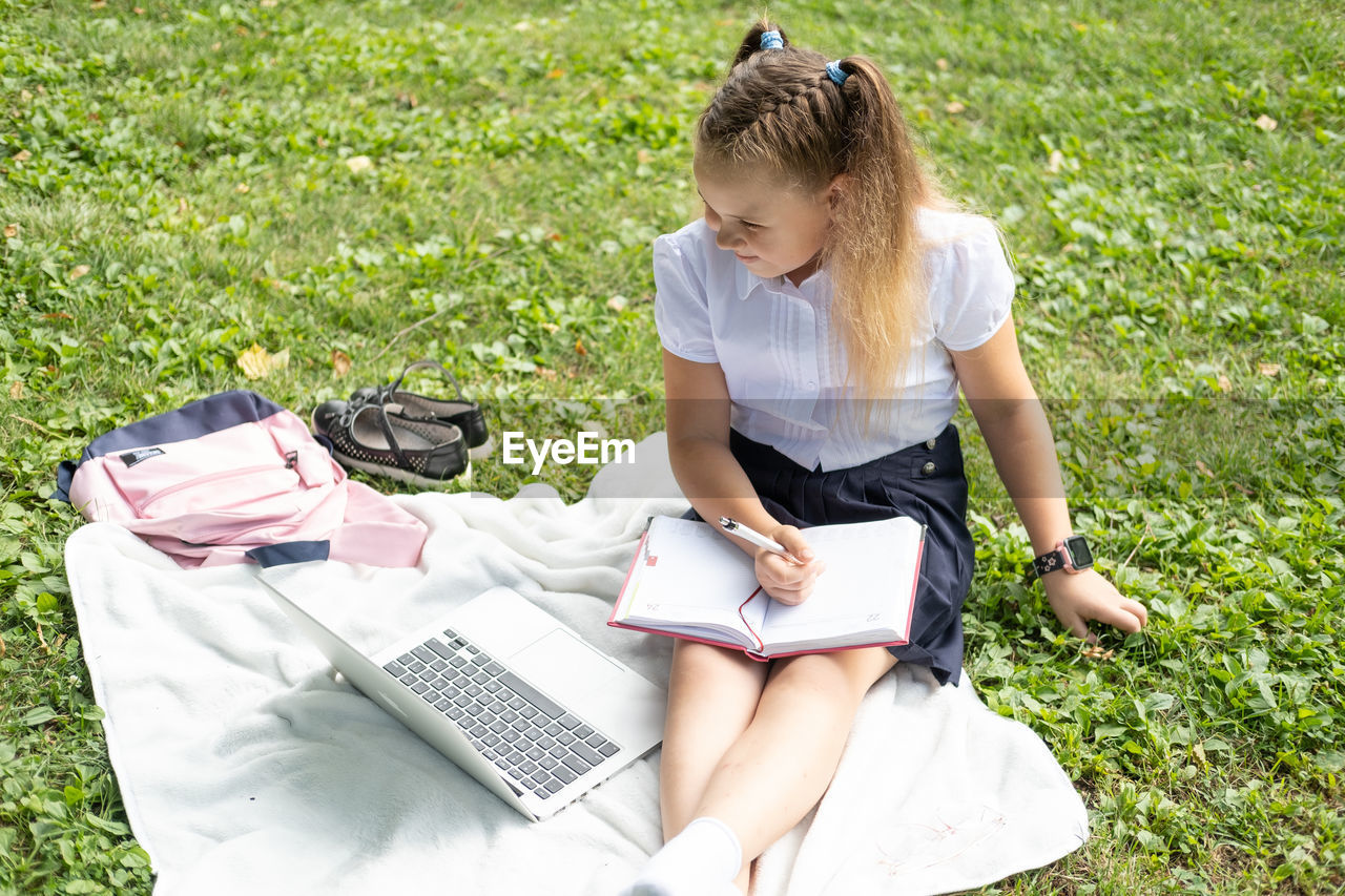 rear view of woman using laptop while sitting on field