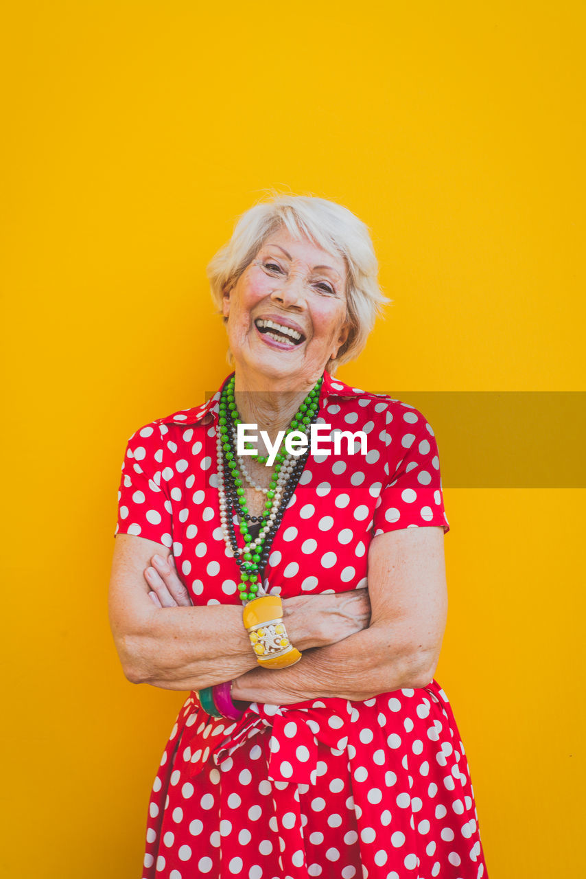 Portrait of smiling senior woman standing against yellow background