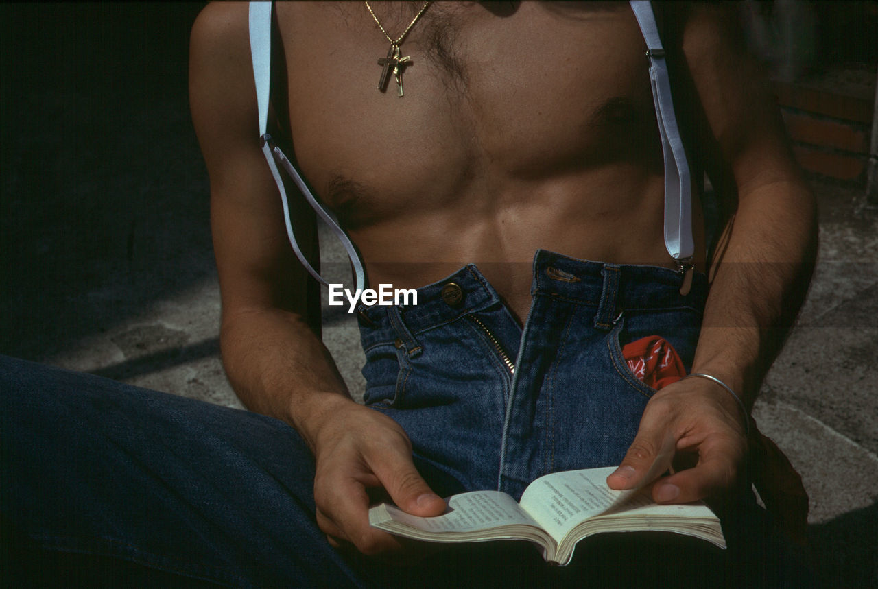 Midsection of shirtless man reading book