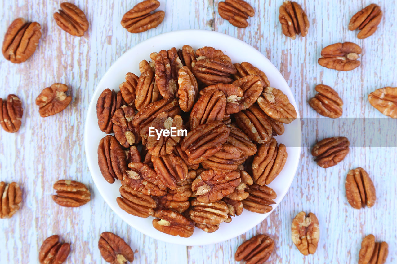 Plate of dried pecan nuts with some kernels scattered on wooden background