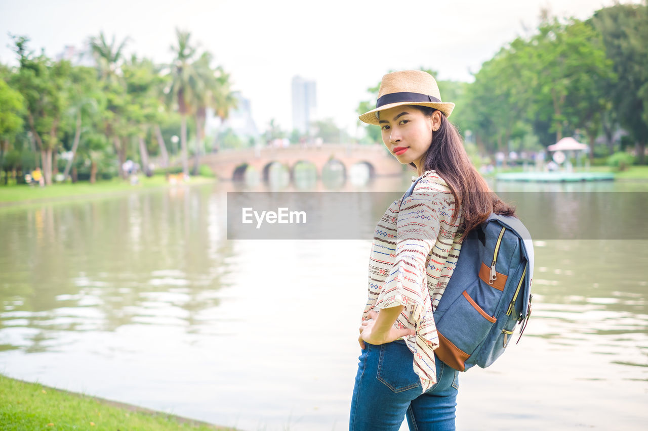 Side view portrait of woman with backpack standing by lake in park