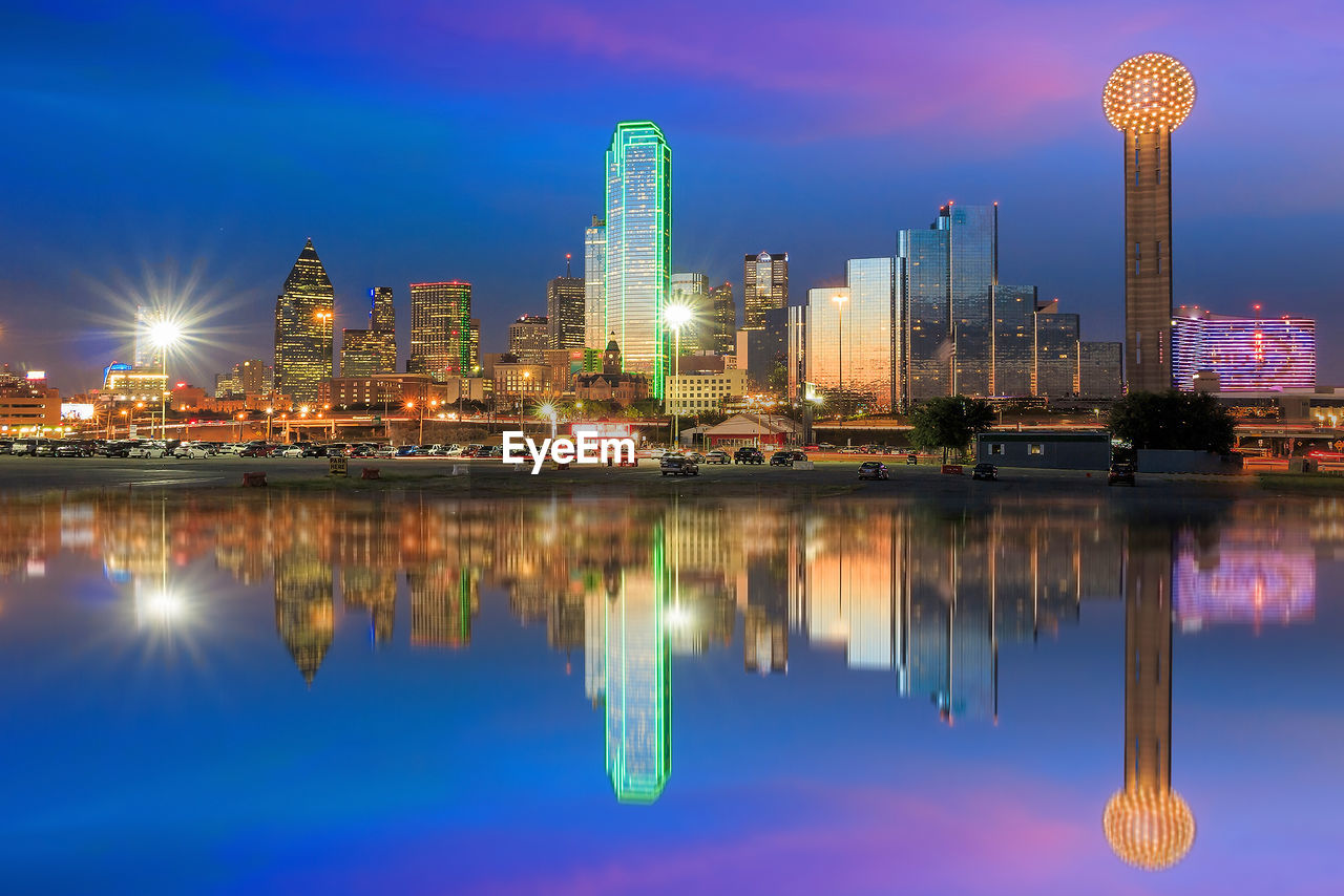 REFLECTION OF ILLUMINATED BUILDINGS IN LAKE AGAINST SKY