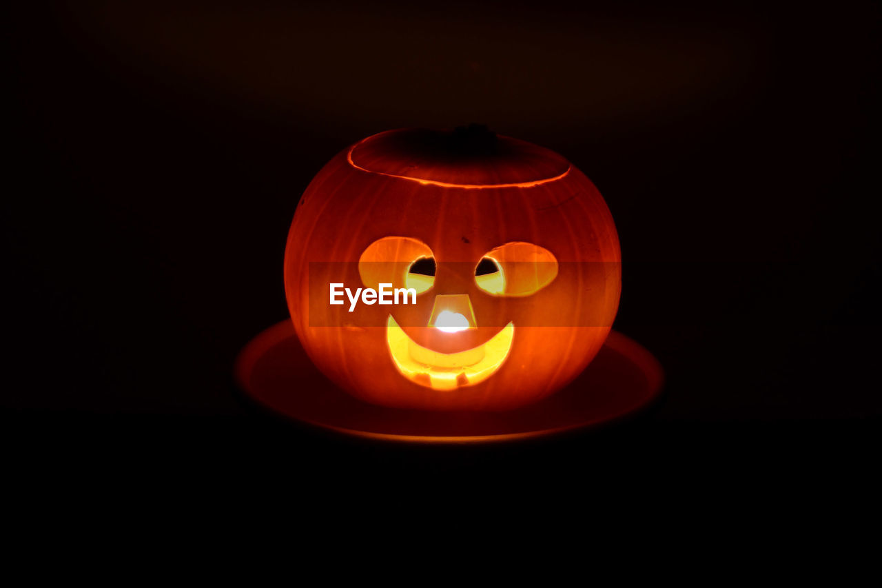 Close-up of illuminated halloween pumpkin on a plate against black background