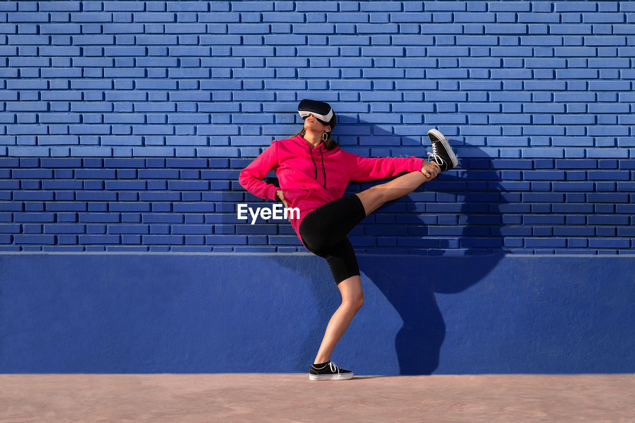 sports, one person, sports clothing, full length, adult, young adult, lifestyles, clothing, exercising, athlete, blue, tennis, vitality, person, footwear, motion, sports training, sports equipment, leisure activity, determination, running, day, racket sport, architecture, wall - building feature, casual clothing, strength, wall, racket, motivation, copy space, standing, outdoors