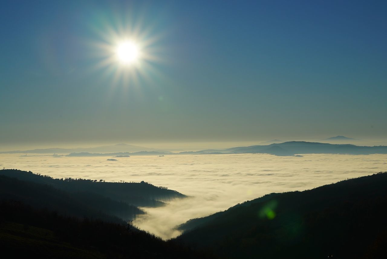 Sun shining over mountains surrounded by clouds