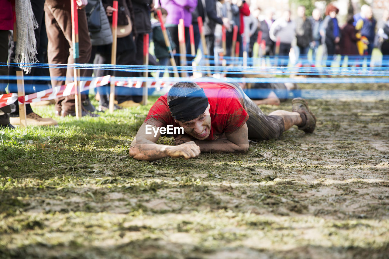 Man crawling under barbed wires on field during race