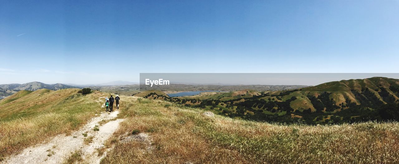 People walking on mountain against clear blue sky